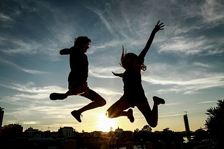 silhouette of two people jumping under blue and white sky thumbnail