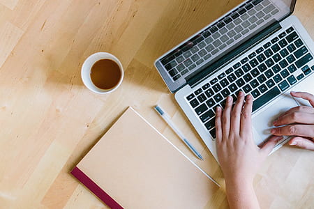 person using gray and black laptop computer beside ball ballpoint pen, white disposable cup and brown notebook thumbnail