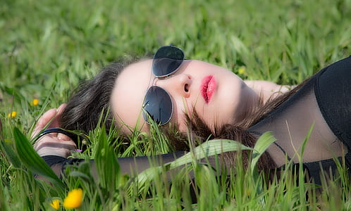 woman wearing black long-sleeved top and black aviator-style sunglasses lying on grass during daytime thumbnail