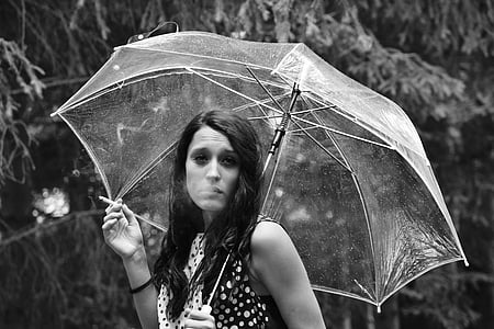 grayscale photo of woman holding umbrella and cigarette stick thumbnail