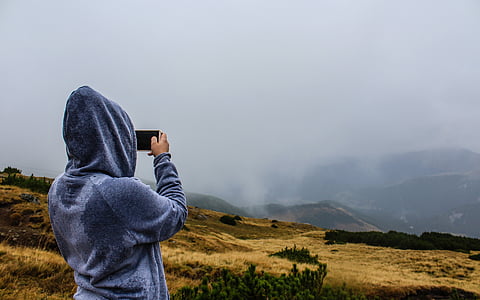 person holding black smartphone taking picture mountain thumbnail