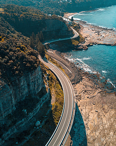 concrete road beside cliff near body of water at daytime thumbnail