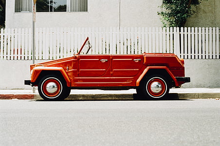 red Volkswagen Thing convertible parked near white fence at daytime thumbnail