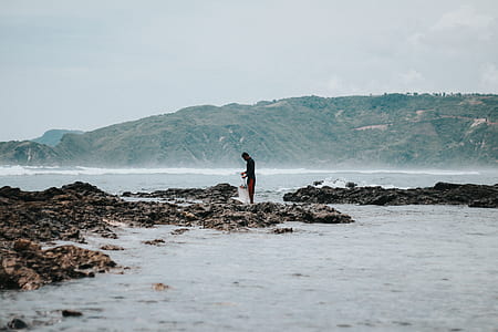 person standing on brown rocks on body of water thumbnail