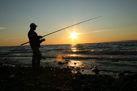 silhouette of person holding fishing rod on beach shore during sunset thumbnail