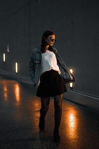 woman walking beside white wall during night thumbnail
