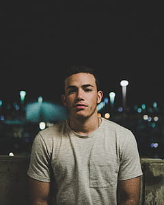man wearing gray crew-neck t-shirt and silver-colored link ball necklace behind gray concrete railings during night time thumbnail