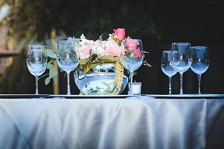 clear wine glasses and red rose flower arrangement on table outdoors during daytime thumbnail