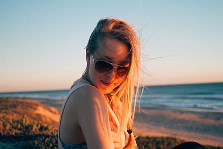 woman wearing white sleeveless shirt and black sunglasses standing on shore thumbnail