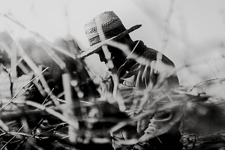 grayscale photo of man wearing hat surrounded by grass thumbnail