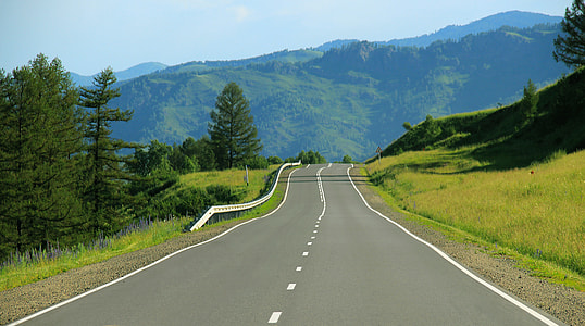 gray concrete road on between green grass and trees near mountain at daytime thumbnail