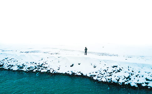 person standing on snowy ground beside body of water thumbnail