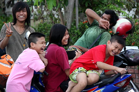 five people smiling on and beside blue motorcycle near green plants thumbnail