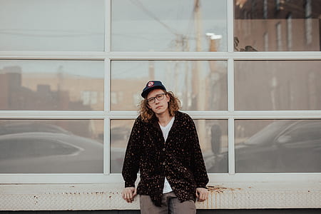 man wearing black jacket leaning on whit wall thumbnail