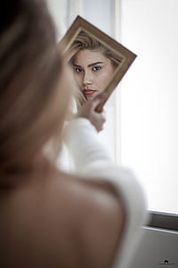 woman wearing white long-sleeved top holding mirror thumbnail