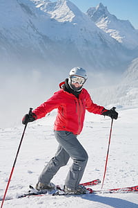 man wearing red zip-up jacket and gray pants with skiblades on snow thumbnail