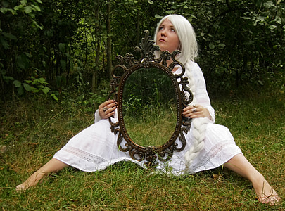 woman wearing white dress holding mirror while sitting on grass at daytime thumbnail