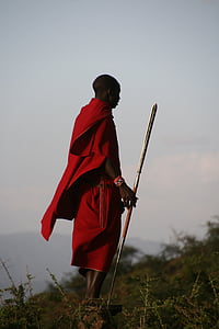man wearing red top and bottoms holding gray metal spear standing on rock during daytime thumbnail