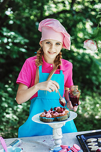girl wearing blue apron designing cupcake during daytime thumbnail