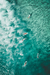 five people surfing on body of water during day time thumbnail