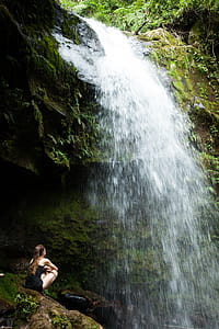 Photo of Woman Sitting on Rock Facing the Waterfalls thumbnail