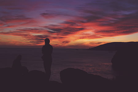 silhouette photo of man standing near rock during golden hour thumbnail