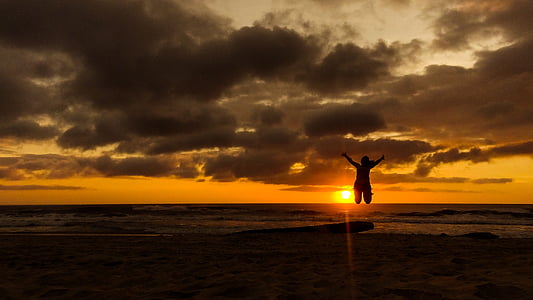 person jumping on seashore during sunset thumbnail
