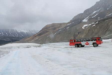 red and white bus traveling on dirt road near mountain thumbnail