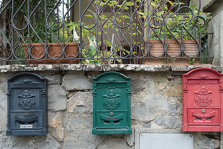 black, green, and red steel mailboxes mounted on gray concrete wall thumbnail