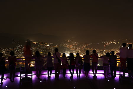 people standing and leaning on railing overlooking city with lights at nighttime thumbnail