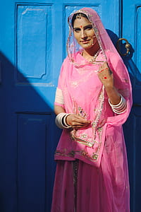 woman in pink sari dress standing in front of blue door during daytime thumbnail