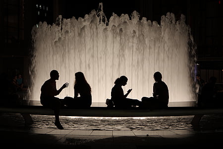 silhouette of four people sitting on bench by the fountain at night thumbnail