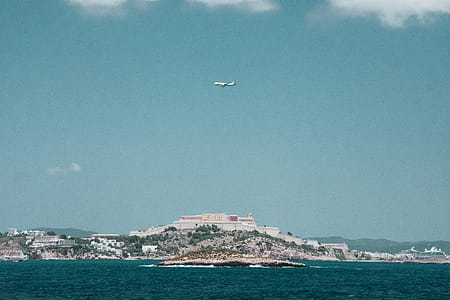 White Airplane Flying over a City Under Blue and White Cloudy Sky thumbnail
