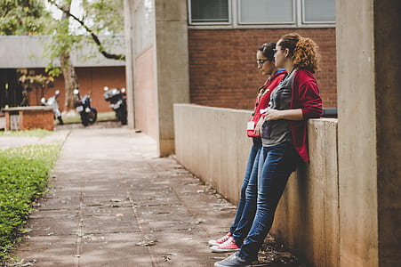 two women leaning on concrete wall thumbnail
