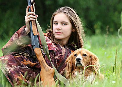 woman with red tree camouflage suit holding brown hunting rifle beside orange and white Welsh springer spaniel on grass field during daytime thumbnail