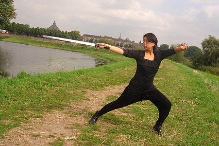 woman in black pants holding sword standing near lake thumbnail