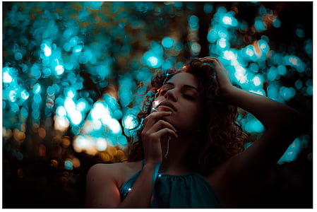 selective focus photography of woman in teal sleeveless top holding white string lights with bokeh brackground thumbnail