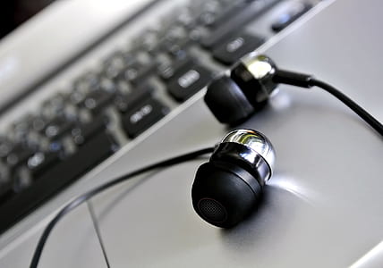 black in-ear earbuds in front of gray laptop computer thumbnail