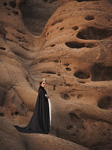woman with crown and black cape standing beside rock wall thumbnail