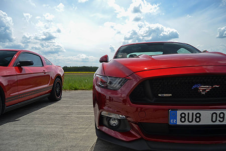 black Ford Mustang beside red coupe parked under white clouds thumbnail