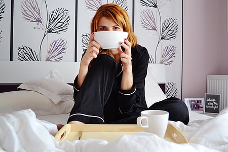 woman in black pajama sitting on bed holding white bowl thumbnail