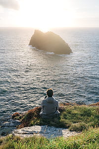 man sitting on grasses near body of water thumbnail