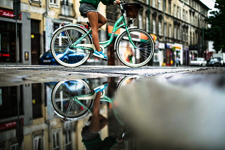 person riding on teal step-through bike beside cconcrete building thumbnail