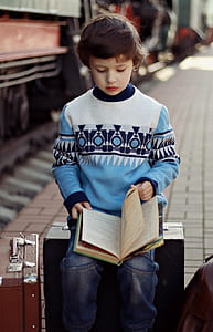 boy wearing multicolored sweater reading and holding book on lap thumbnail