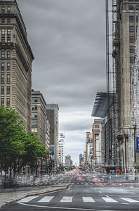 Time Lapse photo of running vehicles on road surrounded by concrete high rise buildings under gray sky during daytime thumbnail