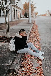man in black coat wearing white backpack sitting on sidewalk during daytime thumbnail