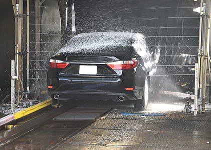 black sedan being washed in a moving car wash during day thumbnail