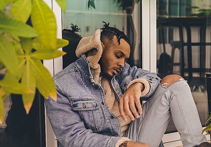 man wearing blue denim hooded jacket sitting beside glass door thumbnail