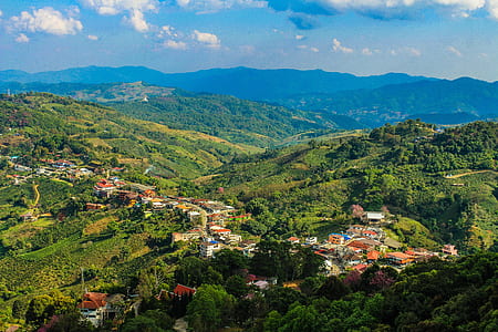 Aerial Photo of City Buildings Beside Green Mountains Under Cloudy Sky thumbnail