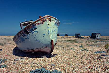 An old abandoned boat lies on a shingle beach on a sunny day. Image captured in Dungeness, Kent, England thumbnail